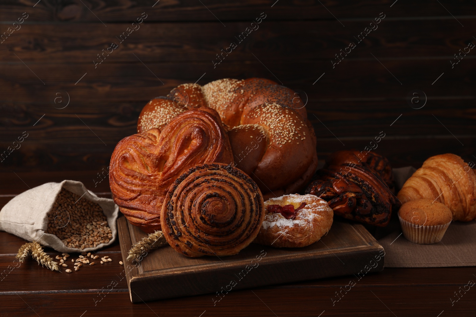 Photo of Different tasty freshly baked pastries and bag with grains on wooden table