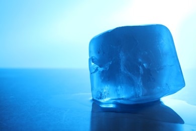 Photo of One crystal clear ice cube on light blue background, closeup and space for text. Color tone effect