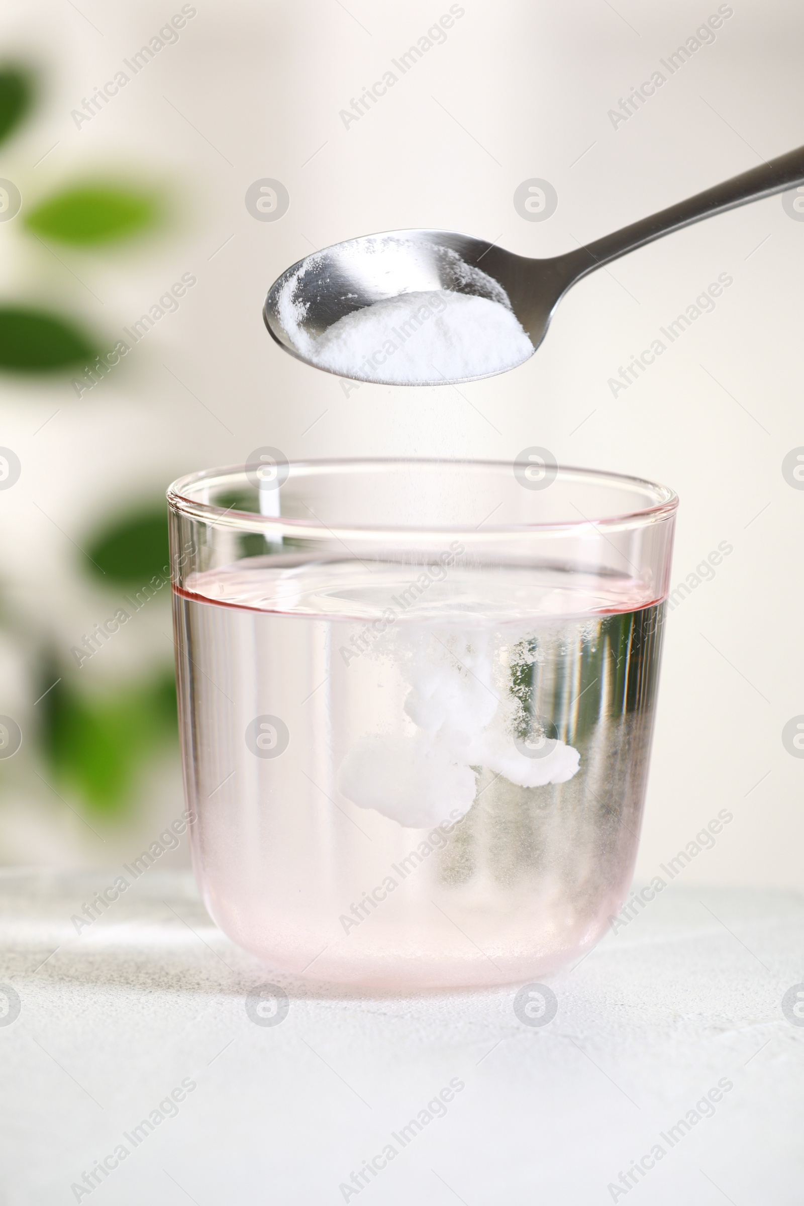 Photo of Adding baking soda into glass of water at white table against blurred background