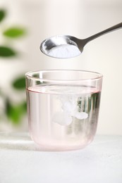 Photo of Adding baking soda into glass of water at white table against blurred background