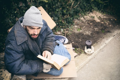 Poor homeless man with book on street in city