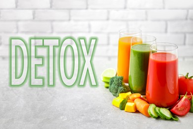 Image of Glasses of delicious juices on grey table against brick wall and word Detox