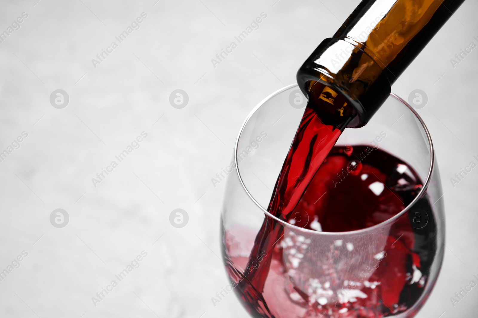 Photo of Pouring red wine from bottle into glass on light background, closeup. Space for text