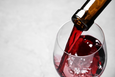 Pouring red wine from bottle into glass on light background, closeup. Space for text