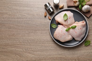 Photo of Raw chicken thighs with basil on wooden table, flat lay. Space for text