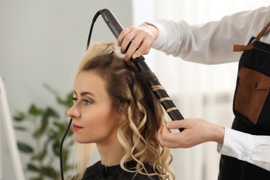 Hair styling. Hairdresser curling woman's hair in salon, closeup