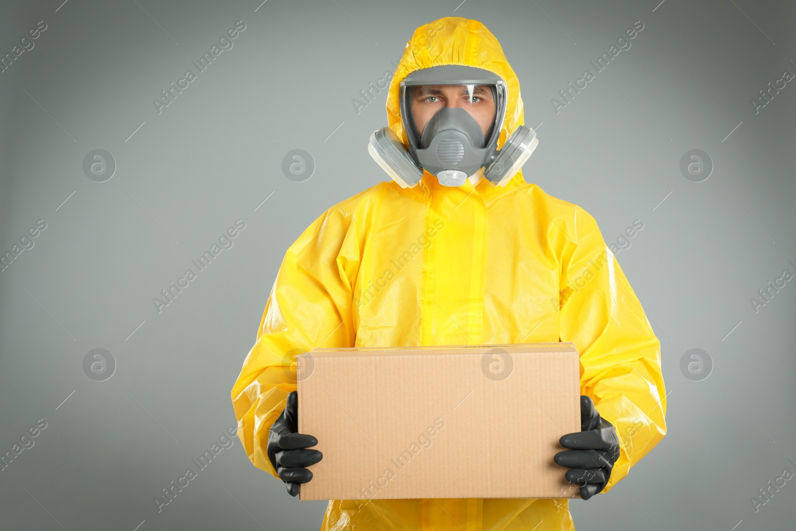 Photo of Man wearing chemical protective suit with cardboard box on light grey background. Prevention of virus spread