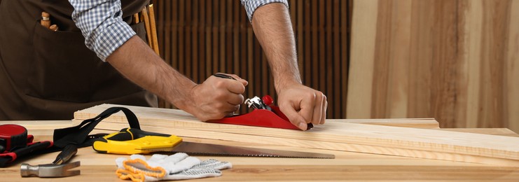 Image of Carpenter working with timber at table indoors, closeup. Banner design