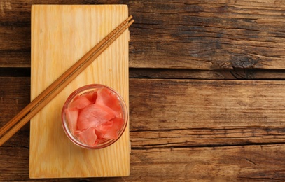 Photo of Spicy pickled ginger and chopsticks on wooden table, top view. Space for text