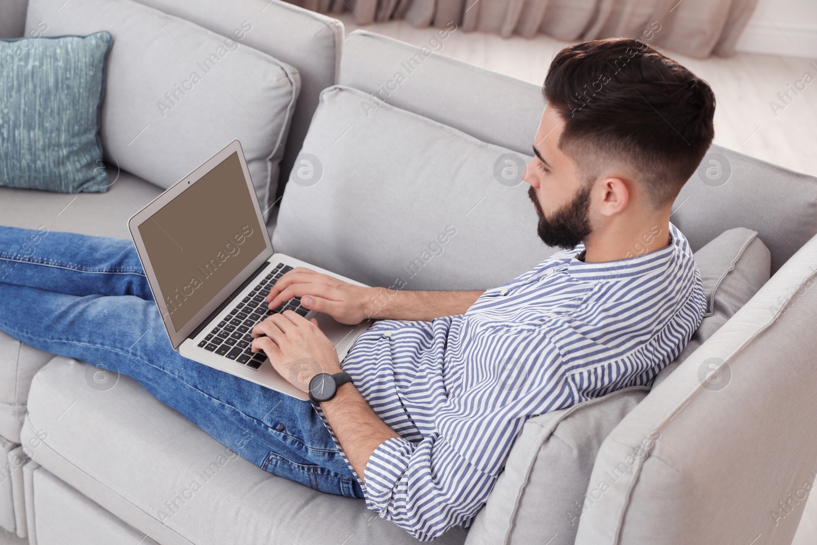 Photo of Handsome young man working with laptop on sofa at home