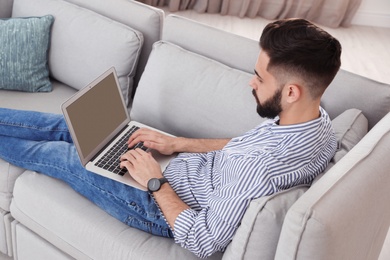 Handsome young man working with laptop on sofa at home