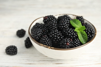 Photo of Bowl of ripe blackberries with mint on white wooden table