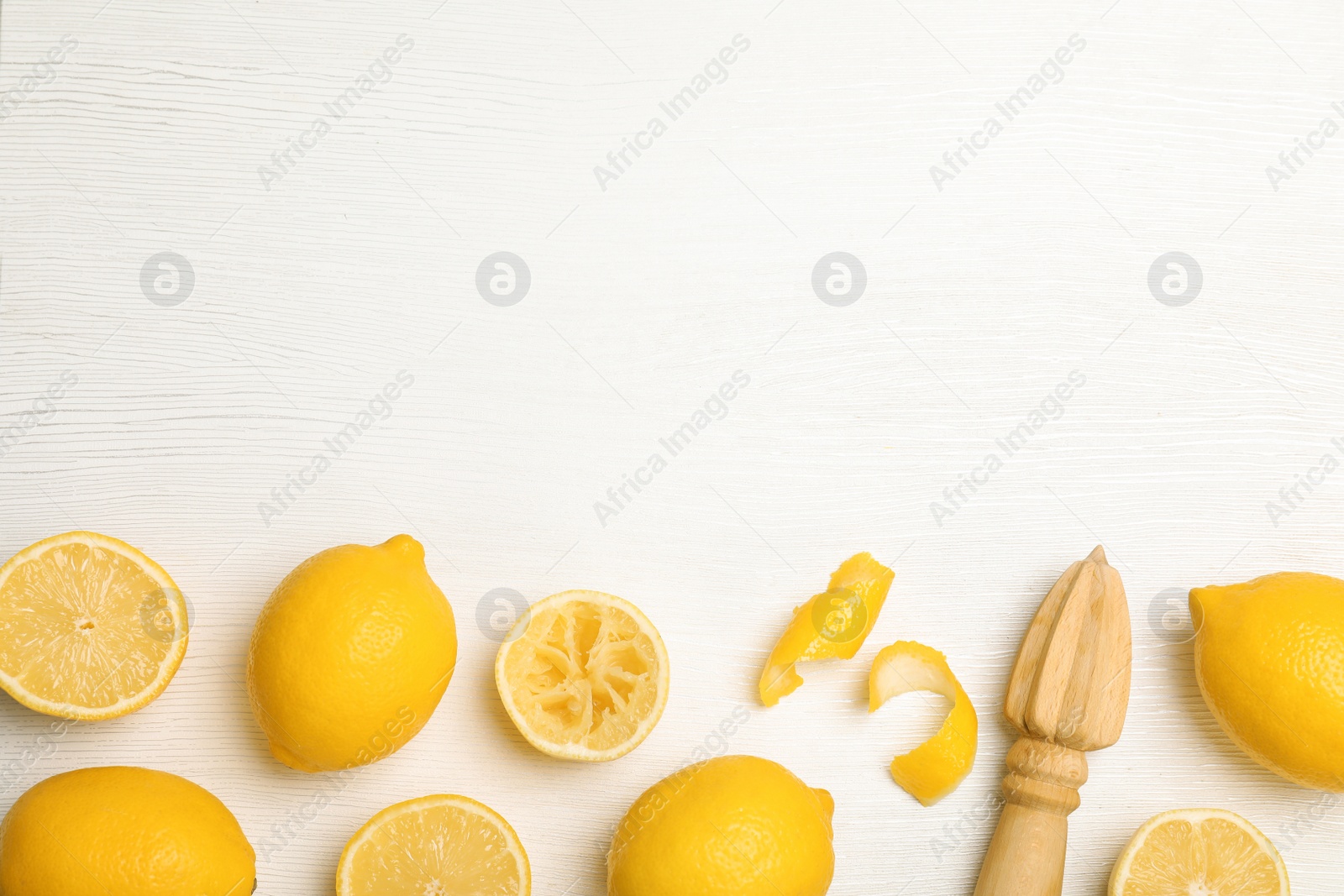 Photo of Composition with reamer and fresh lemons on white wooden background, top view. Space for text