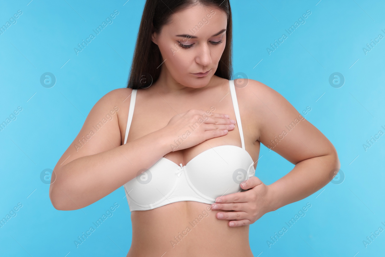 Photo of Mammology. Woman in bra doing breast self-examination on light blue background