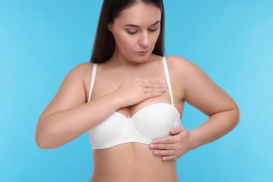 Mammology. Woman in bra doing breast self-examination on light blue background