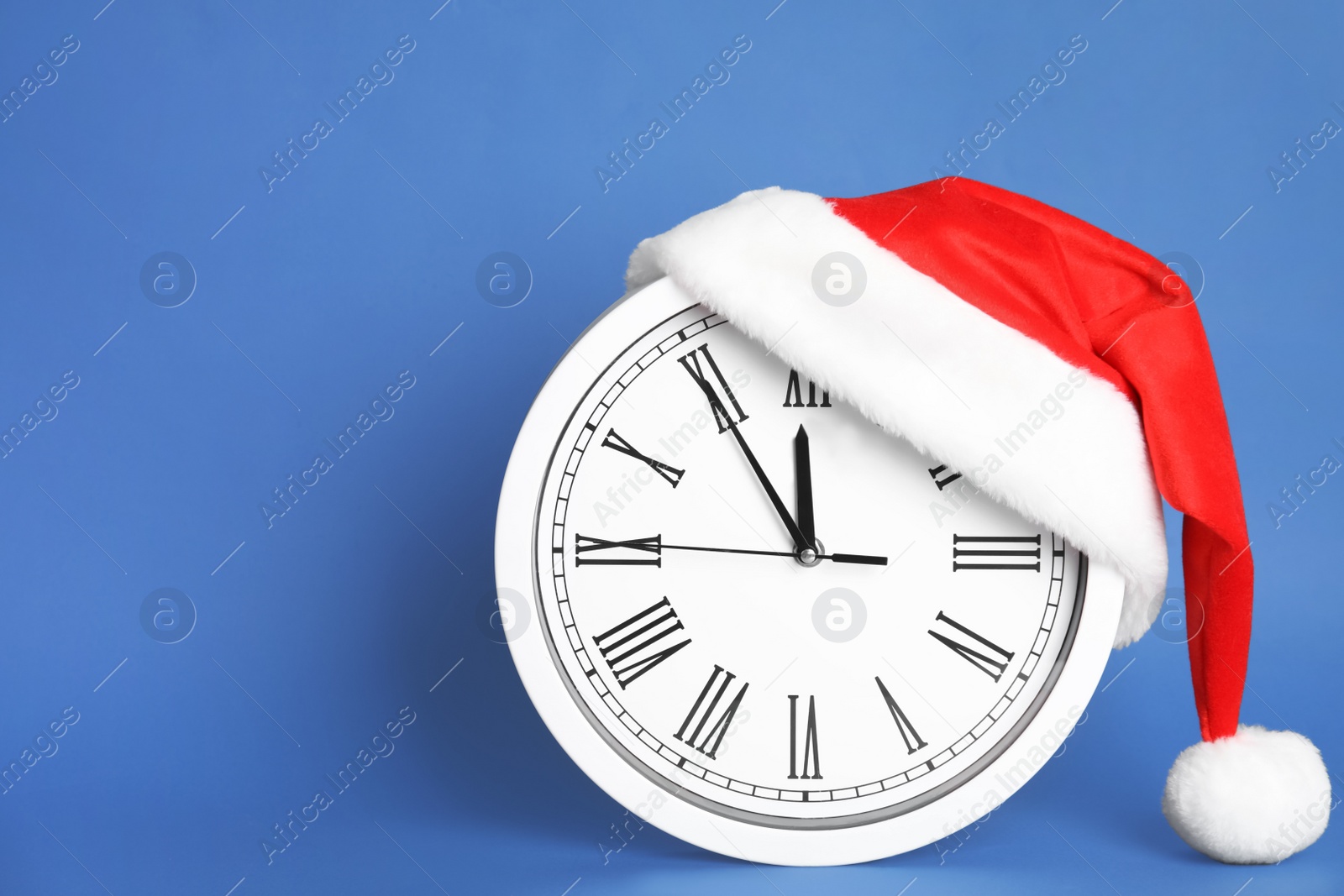 Photo of Clock with Santa hat showing five minutes until midnight on blue background, space for text. New Year countdown