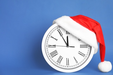 Photo of Clock with Santa hat showing five minutes until midnight on blue background, space for text. New Year countdown