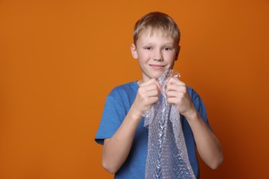 Boy popping bubble wrap on orange background, space for text. Stress relief
