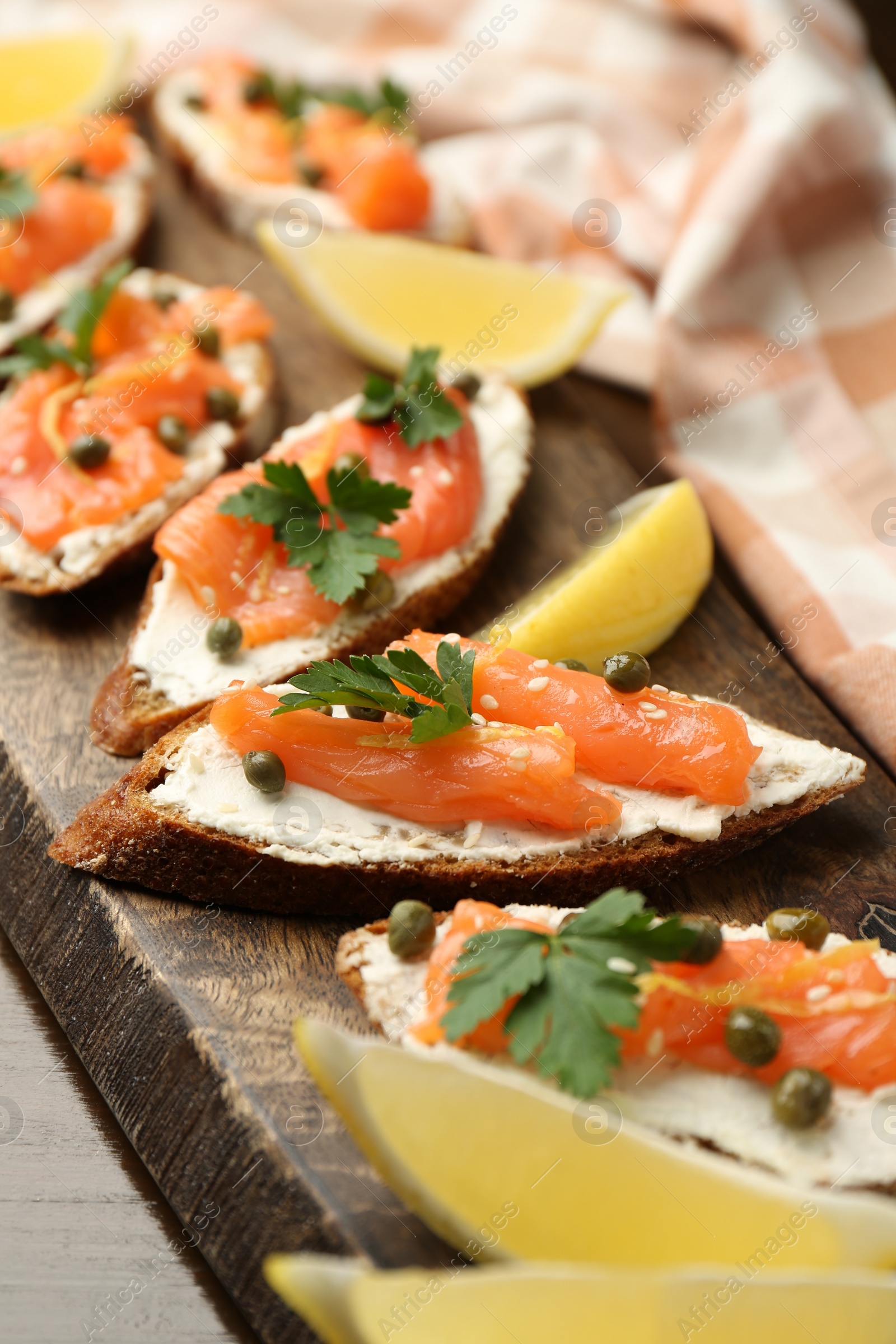 Photo of Tasty canapes with salmon, capers, lemon and cream cheese on wooden table, closeup