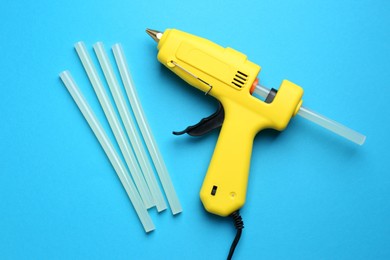 Yellow glue gun and sticks on light blue background, flat lay