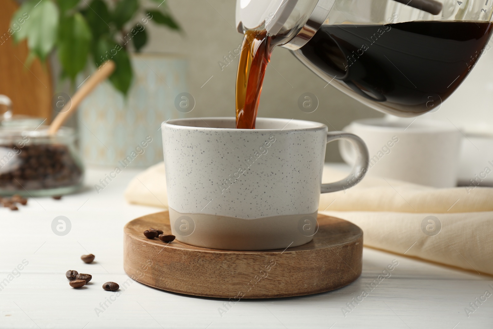 Photo of Pouring coffee into cup at white wooden table, closeup