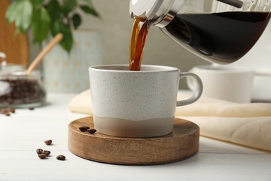 Pouring coffee into cup at white wooden table, closeup