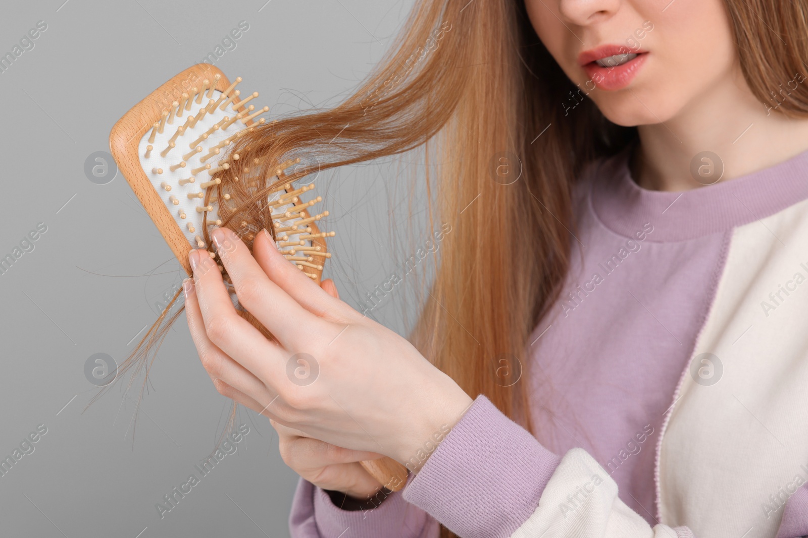 Photo of Woman brushing her hair on light grey background, closeup. Alopecia problem