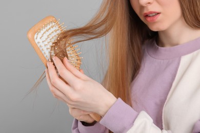 Photo of Woman brushing her hair on light grey background, closeup. Alopecia problem