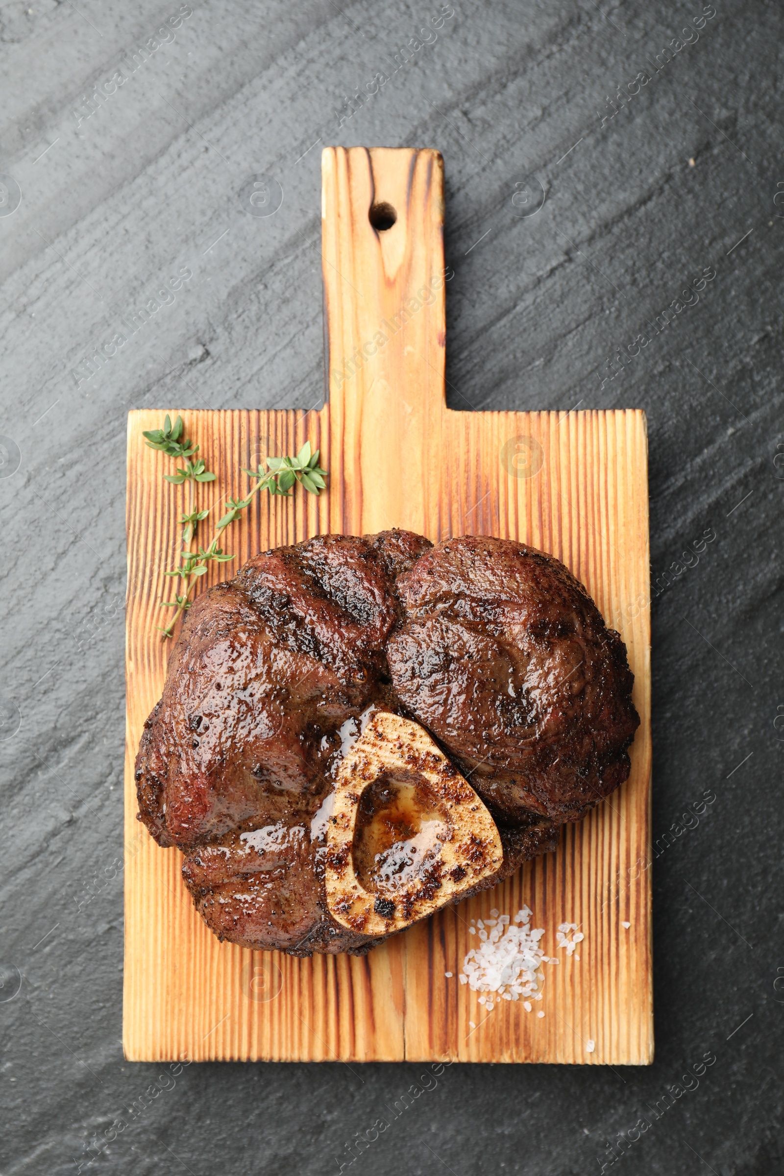 Photo of Piece of delicious grilled beef meat, thyme and salt on black table, top view