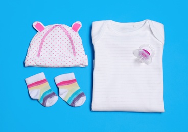 Flat lay composition with baby clothes and pacifier on blue background