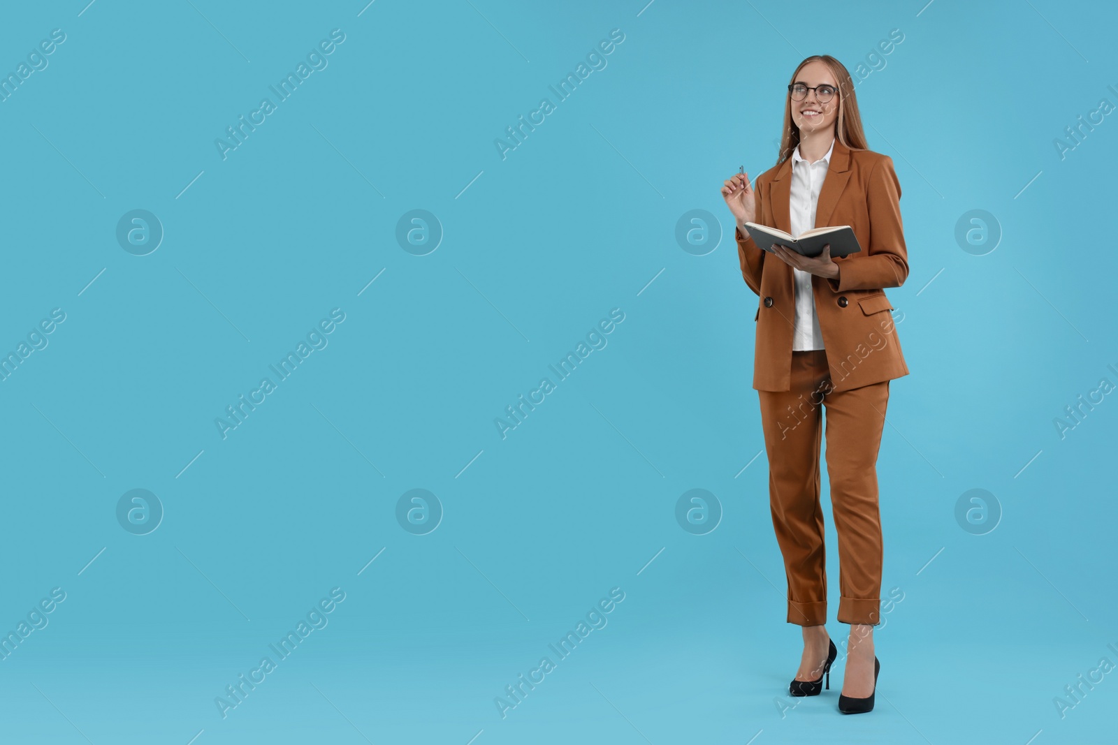 Photo of Happy young secretary with notebook and pen on light blue background, space for text