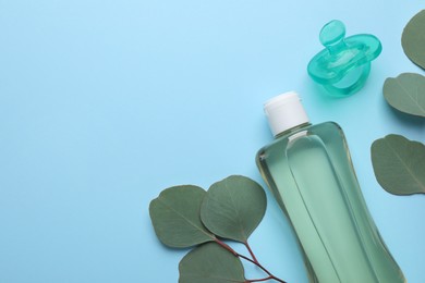 Photo of Bottle of baby oil, pacifier and eucalyptus leaves on light blue background, flat lay. Space for text