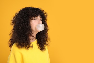 Beautiful young woman blowing bubble gum on orange background. Space for text