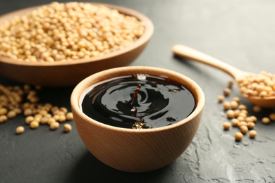 Photo of Tasty soy sauce in bowl and soybeans on black table, closeup