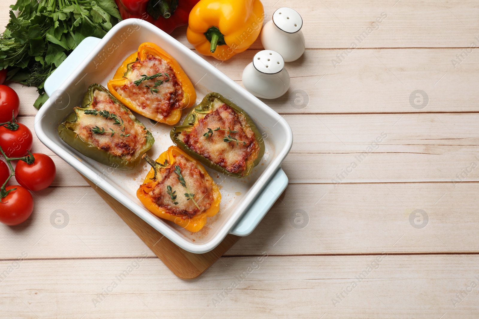 Photo of Tasty stuffed peppers in dish and ingredients on wooden table, flat lay. Space for text