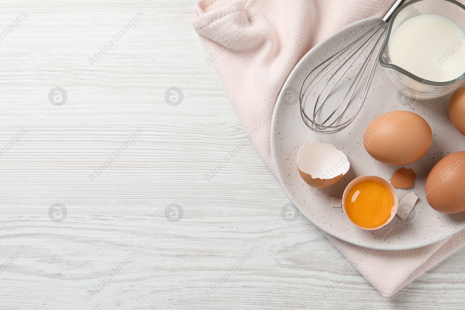 Photo of Chicken eggs, whisk and milk on white wooden table, top view. Space for text