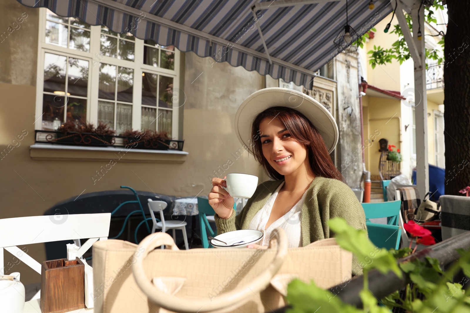 Photo of Young woman with stylish bag at table in outdoor cafe