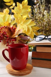 Cup with hot drink, stack of books and viburnum on white wooden windowsill indoors. Autumn atmosphere