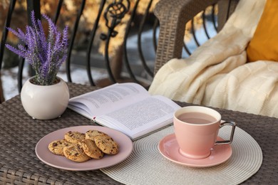 Photo of Cup with tasty cocoa, cookies and book on rattan table at balcony