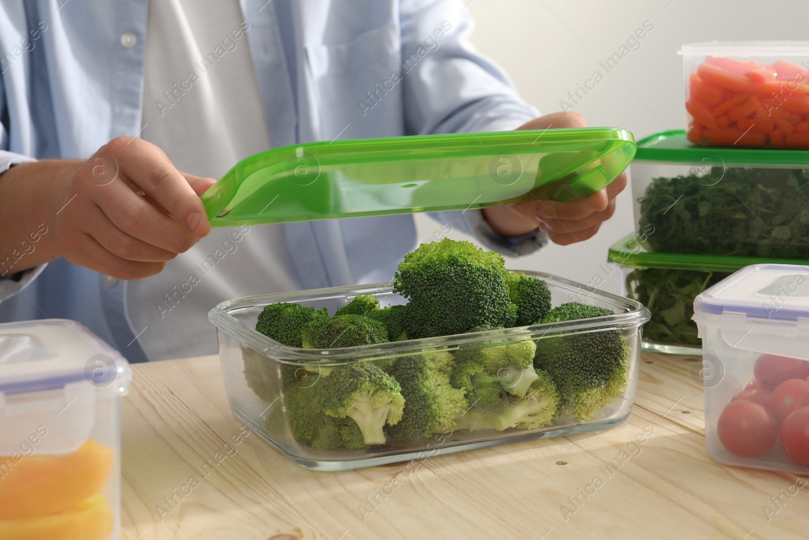 Photo of Man closing glass container with lid at wooden table, closeup. Food storage