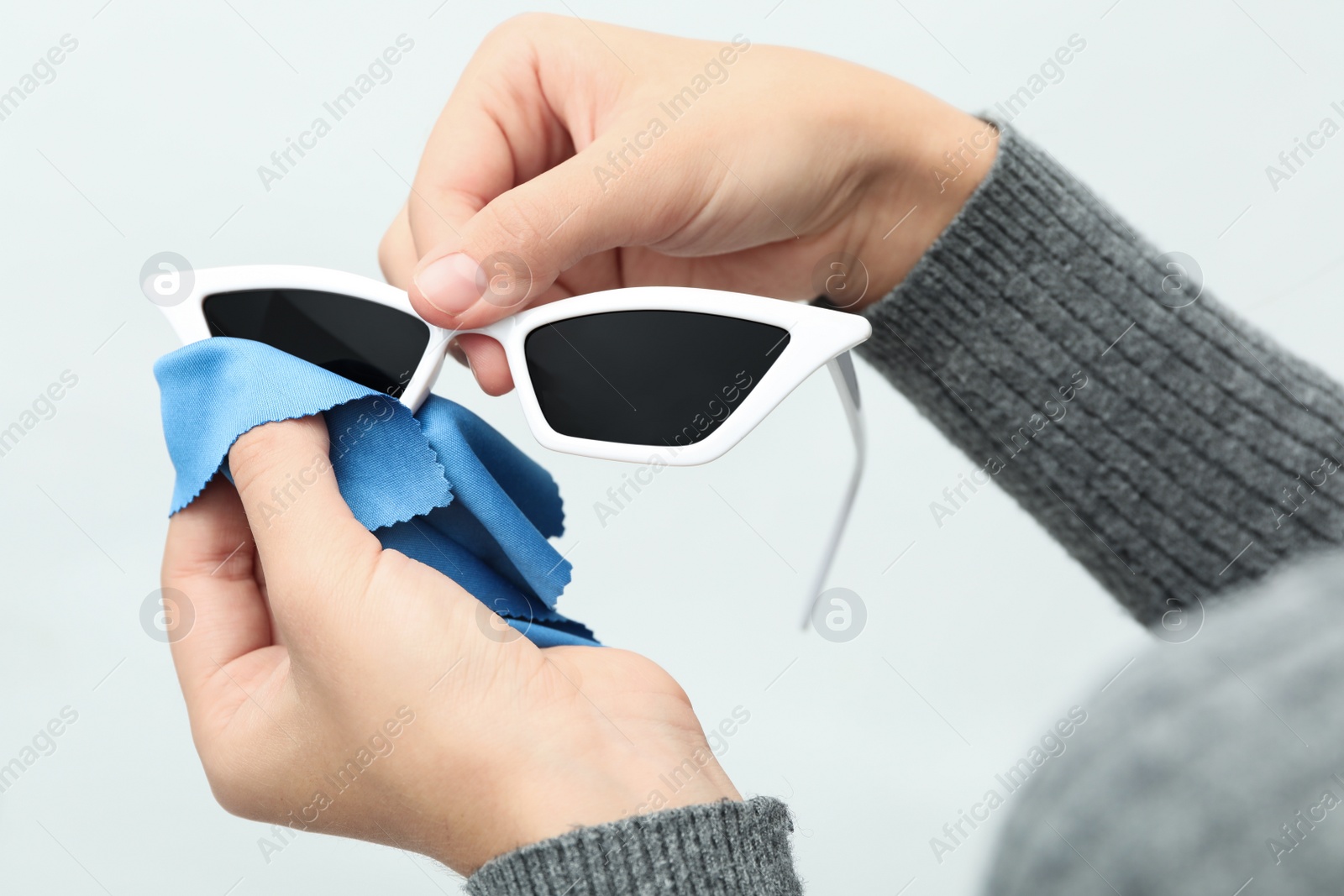 Photo of Woman wiping sunglasses with microfiber cleaning cloth on light background, closeup