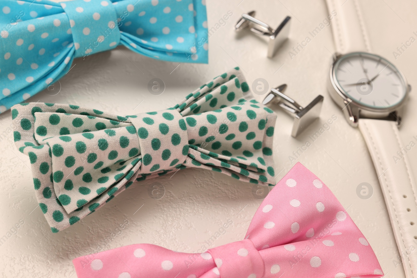 Photo of Stylish color bow ties, wristwatch and cufflinks on white background, closeup