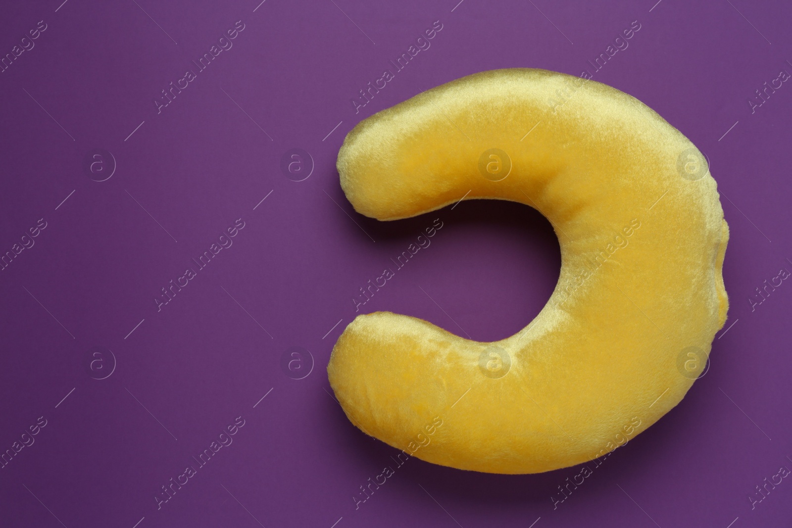 Photo of Yellow travel pillow on purple background, top view. Space for text