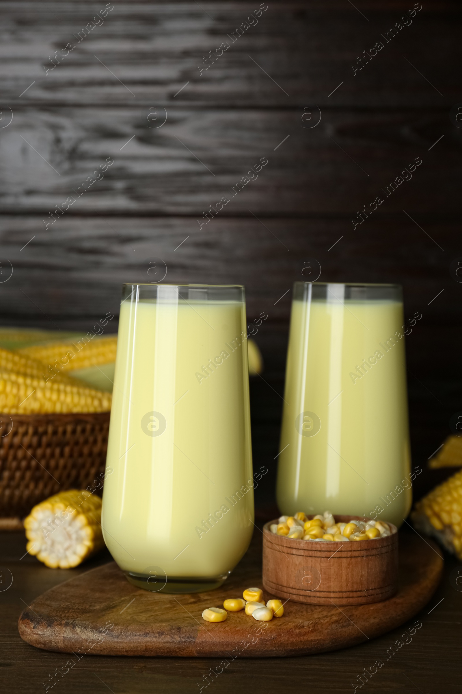 Photo of Tasty fresh corn milk in glasses and cobs on wooden table