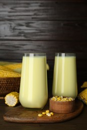 Photo of Tasty fresh corn milk in glasses and cobs on wooden table
