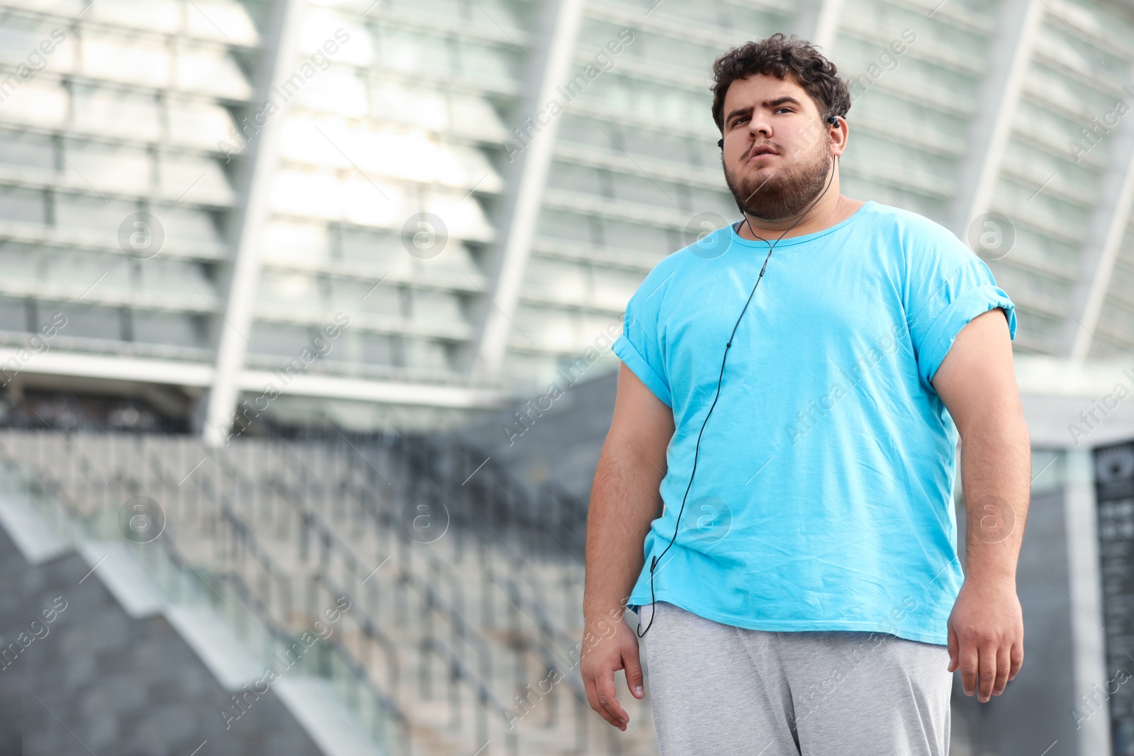 Photo of Young overweight man wearing earphones training outdoors