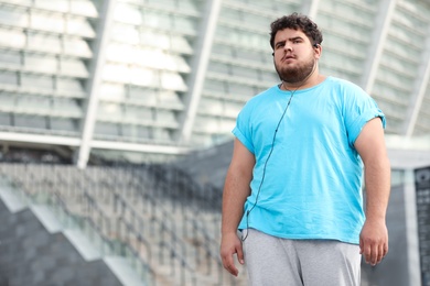 Young overweight man wearing earphones training outdoors