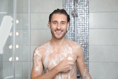 Attractive young man taking shower with soap in bathroom