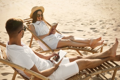 Photo of Young couple relaxing in deck chairs on sandy beach