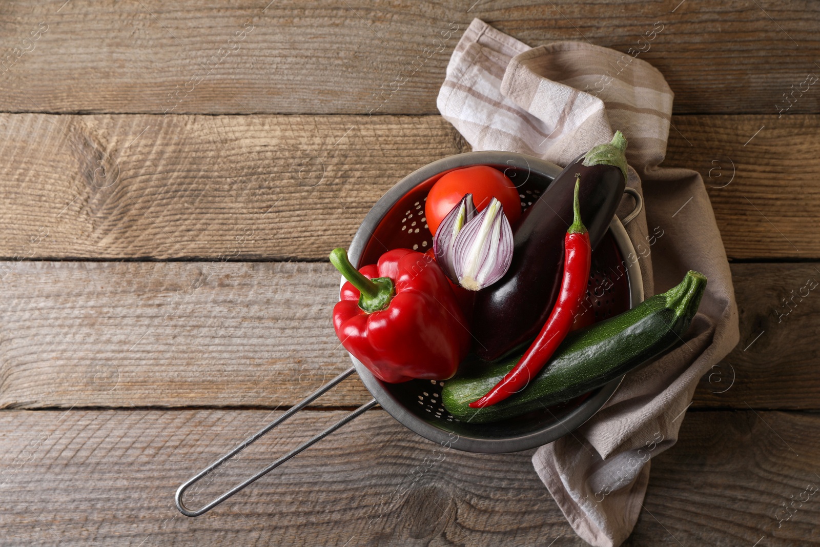 Photo of Fresh vegetables for ratatouille in colander on wooden table, flat lay. Space for text